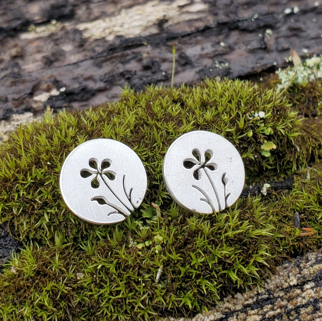 Silver floral earrings on a piece of moss
